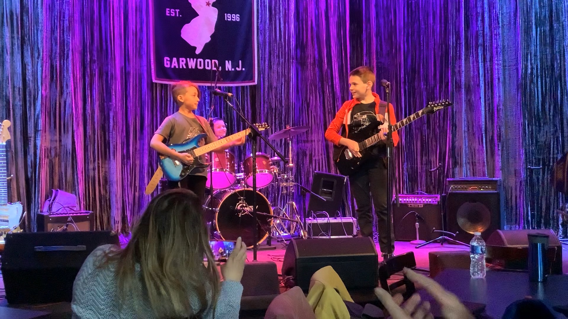 Two young NJWA guitarists playing side by side on a club stage with purple stage lighting