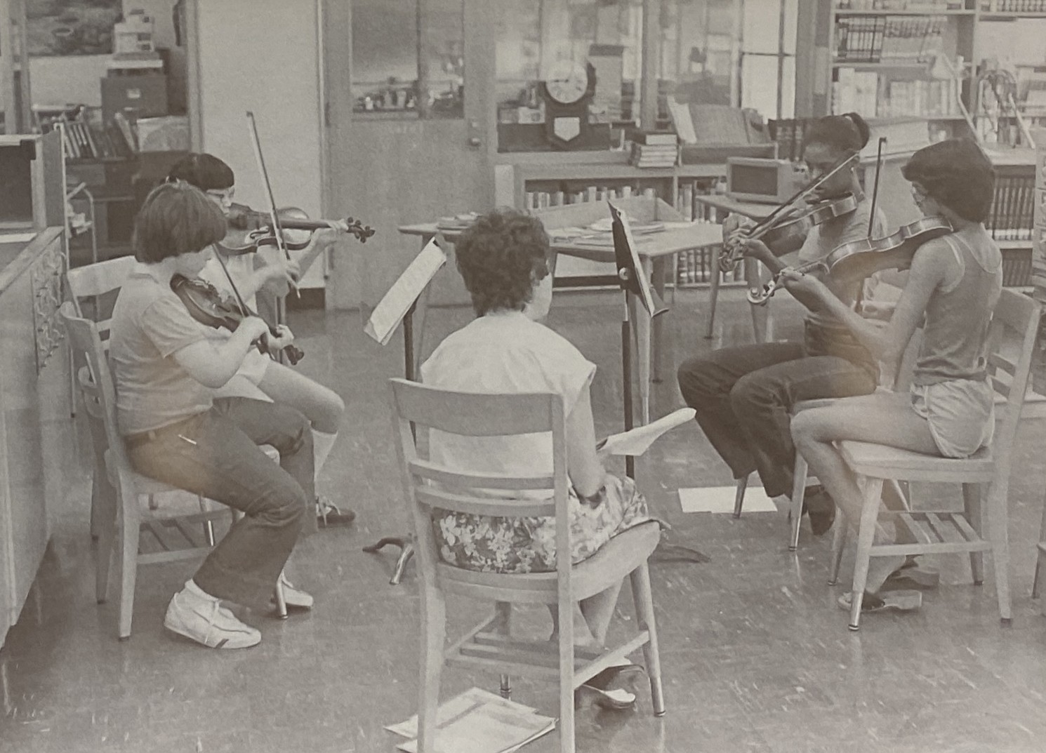 A coach leading a string sectional rehearsal, young violinists seated in a circle with their music stands
