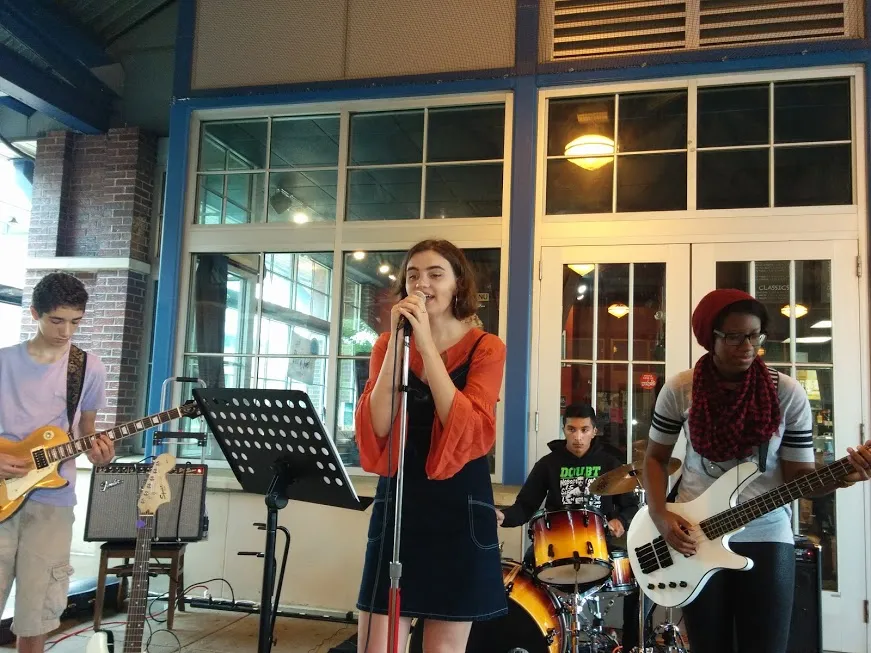 A teen band rehearsing — vocalist at the microphone with guitar, bass and drums