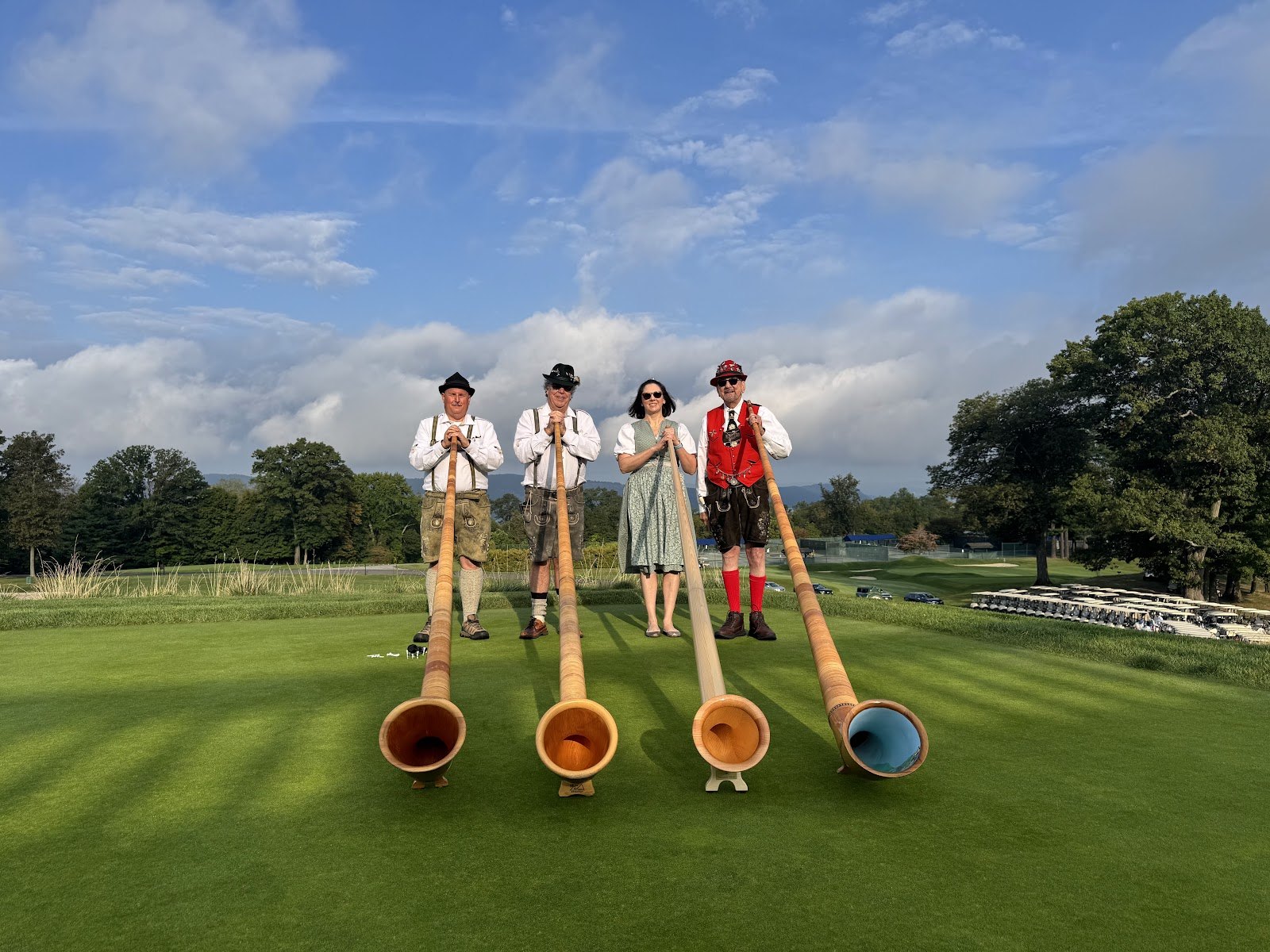 Four NJWA alphorn players in traditional dress on a green lawn with their alphorns