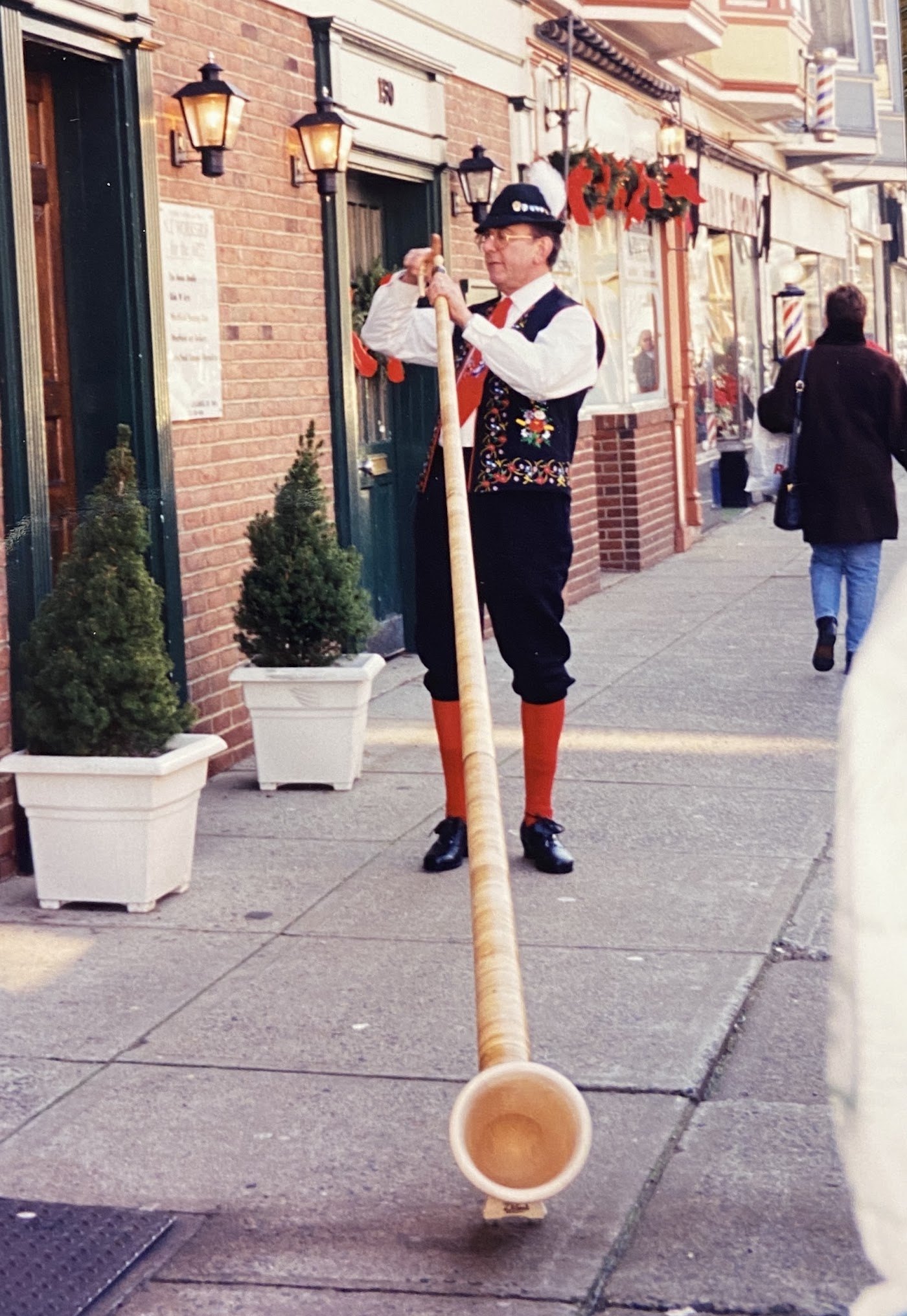 A player in traditional dress sounding a solo alphorn on a downtown sidewalk