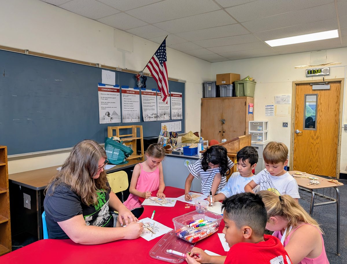 Children drawing together at a classroom table with their teacher