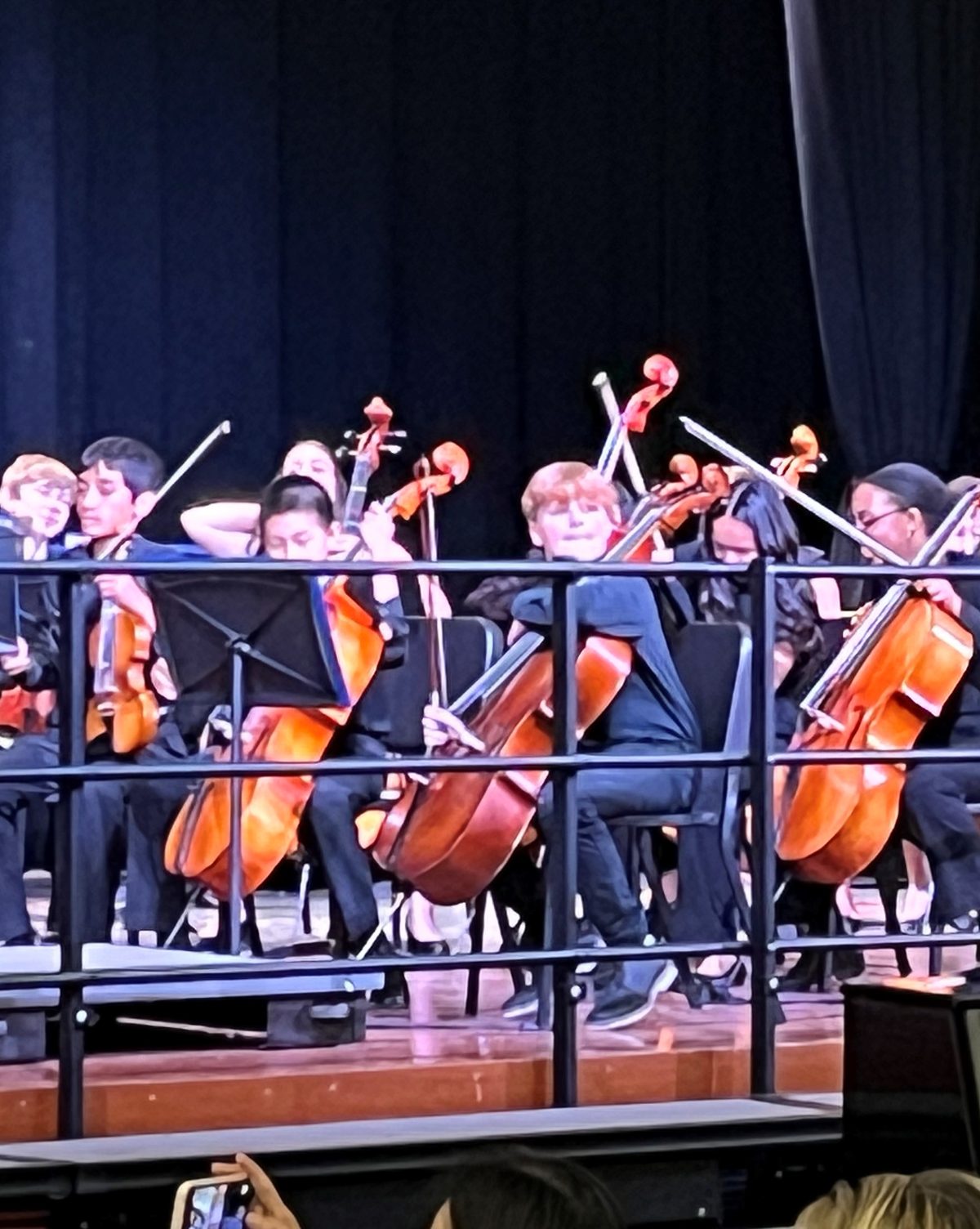 A student orchestra of cellos and violins performing on stage