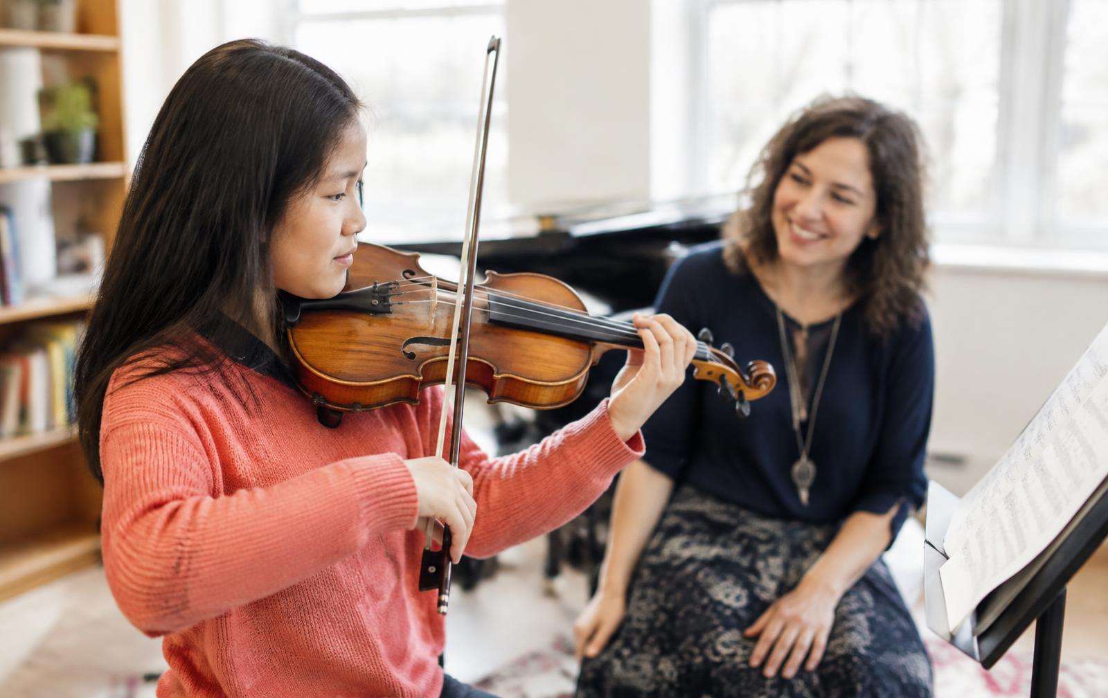 A student playing violin with her teacher in a bright studio