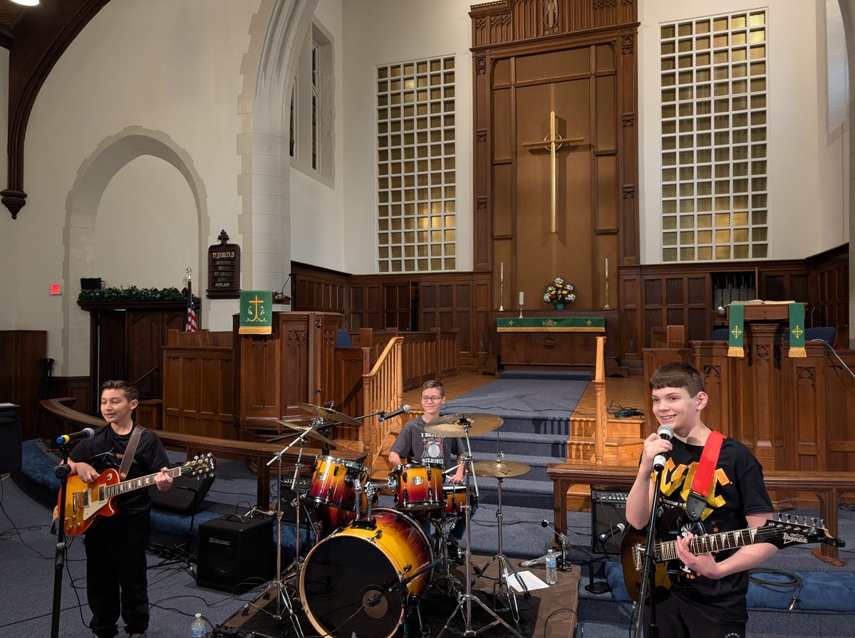 A student rock band performing with guitars and drums in a church hall